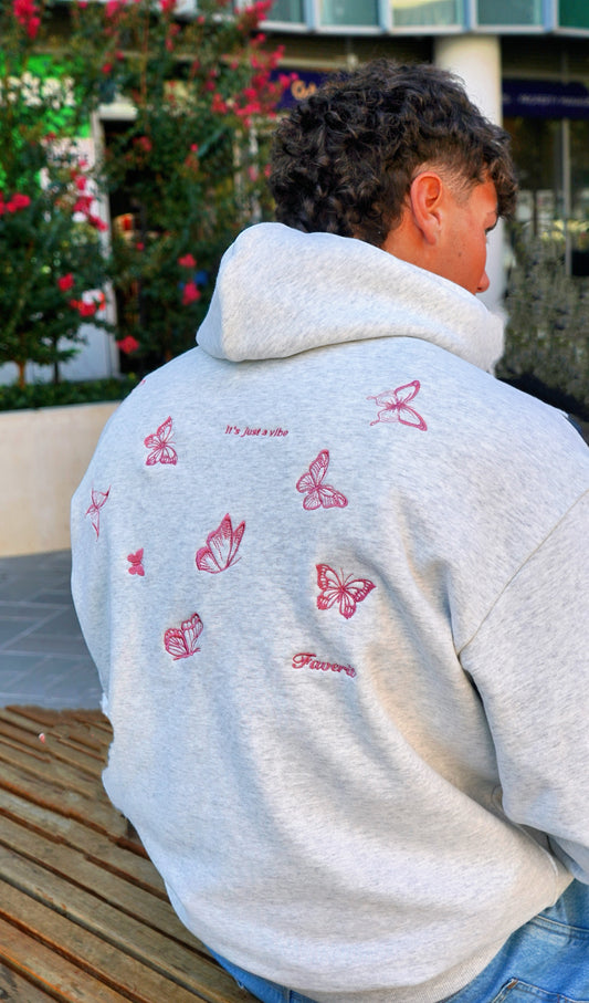 Model wearing heather grey hoodie with butterflies embroidered on it